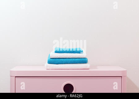 On a pink dresser there is a stack of white and blue towels. Stock Photo