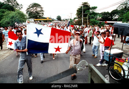 Flag-waving supporters of GEN Manuel Noriega confront a Marine patrol from Company B, 2nd Light Armored Infantry Battalion.  The crowd filled the streets and formed a roadblock with two buses, which can be seen in the background.  Nearby Panamanian Defense Force (PDF) soldiers, two of whom are standing to the right of the flag in the foreground, refused to disperse the crowd and the Marines took another route to complete their patrol. Stock Photo