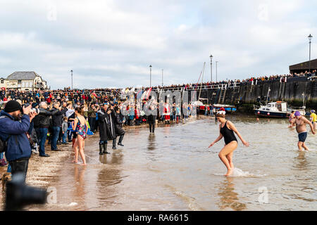People in swim wear, wading back to the beach from the sea after the traditional new Year Day dip or swim, a yearly charity event, at Viking Bay beach, Broadstairs. Crowd of spectators watching from the beach. Stock Photo