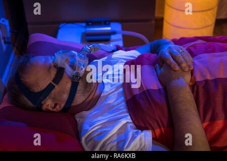 Man with sleep apnea syndrome, wears a CPAP mask while sleeping, breathing mask, which pushes air into the respiratory tract due Stock Photo