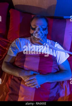 Man with sleep apnea syndrome, wears a CPAP mask while sleeping, breathing mask, which pushes air into the respiratory tract due Stock Photo