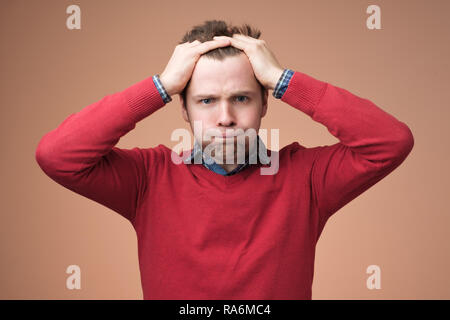 young man in red sweater squeezing head with hands, suffering from stress Stock Photo