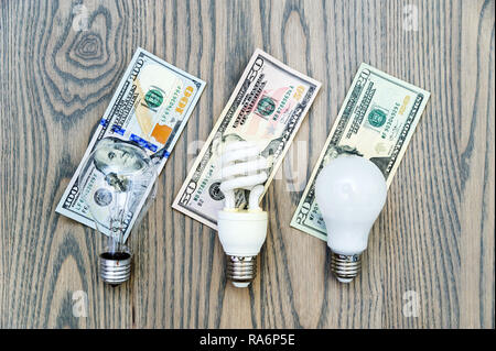 LED bulb saves money. The photo shows three lights: LED, fluorescent and incandescent. Money bills related costs for energy consumption. Stock Photo