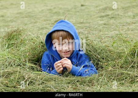 Young boy lying in the hay, Muhle, Schalksmühle, North Rhine-Westphalia, Germany Stock Photo