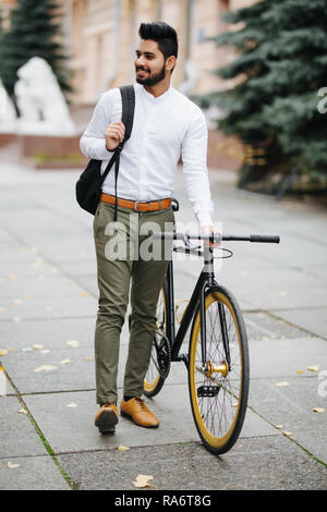 Young handsome asian man with backpack walking down the street pushing bicycle while going to work. Stock Photo