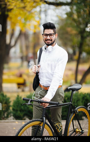 Indian bearded student man with backpack with bicycle walking on street Stock Photo