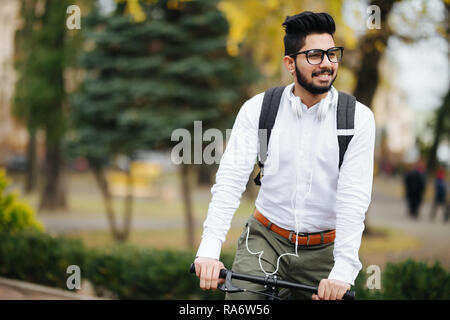 Indian bearded student man with backpack with bicycle walking on street Stock Photo