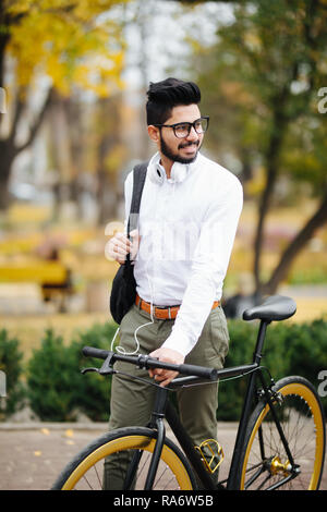 Indian bearded student man with backpack with bicycle walking on street Stock Photo