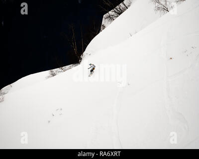 freerider snowboarder down the steep slope of white snow and trees in the mountains of the Caucasus Stock Photo