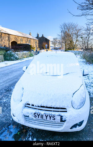 Close-up of snow covered car parked on icy main street of small, scenic rural village on cold, snowy winter day - Timble, North Yorkshire, England, UK Stock Photo