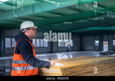 Portrait of development supervisor wearing protective vest and helmet proofing blueprints using a digital tablet inside unfinished building Stock Photo