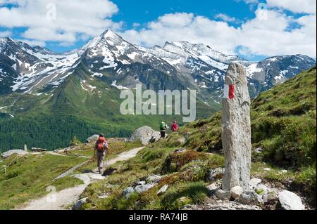 Three hikers on hiking trail, red and white markings on stone, snow-covered mountains, near the Waldner Alm, Kasern, Casere Stock Photo