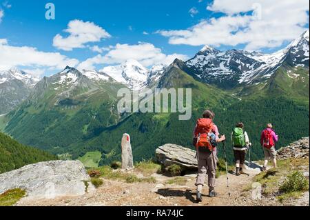 Three hikers hike on a hiking trail, red and white markings on stone, snow-covered mountains, near the Waldner Alm, Kasern Stock Photo