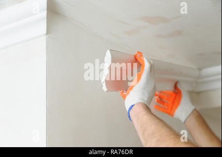 Installation of ceiling moldings. Worker fixes the plastic molding to the ceiling. Stock Photo