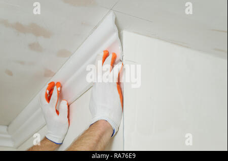 Installation of ceiling moldings. Worker fixes the plastic molding to the ceiling. Stock Photo