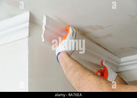 Installation of ceiling moldings. Worker fixes the plastic molding to the ceiling. Stock Photo