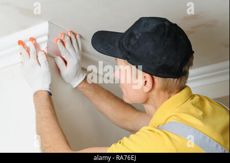 Installation of ceiling moldings. Worker fixes the plastic molding to the ceiling. Stock Photo