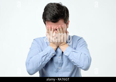 Man covering face with hand while standing against grey background Stock Photo