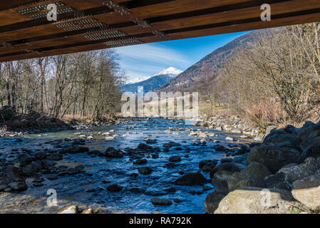 Under the bridge. Mountain river, snow-covered mountains, alpine mountain peak covered with snow. On background Italian village, Trentino Alto Adige Stock Photo