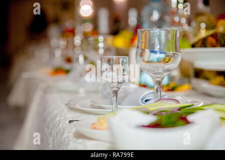Festive tableware with glasses on a table. Empty glasses stand near plates and forks on banquet table decorated with white tablewear. Festively served Stock Photo
