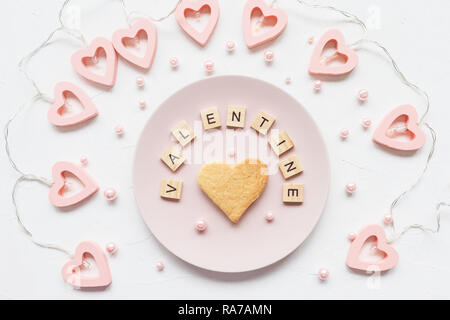 VALENTINE word and heart shaped butter cookie on a pink plate and Valentine's Day decoration - heart shaped lights on a white background Stock Photo