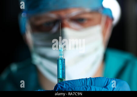 Physician injector arms in sterile uniform holding syringe Stock Photo