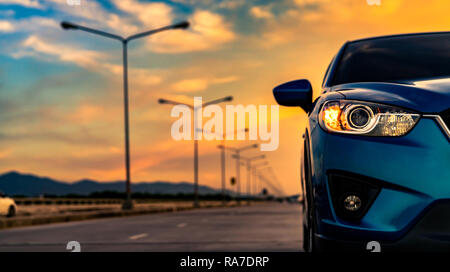 Blue compact SUV car open headlamp light parked on concrete road near the mountain at sunset with beautiful sky and clouds. Road trip travel. Automoti Stock Photo