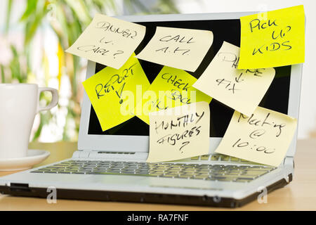 Laptop screen covered with sticky notes with different appointments on brown wooden desk in office - over-worked or too much work concept Stock Photo
