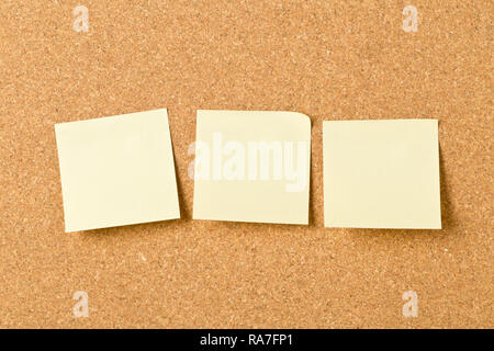 Three empty yellow sticky paper memo notes on cork board with copy space Stock Photo