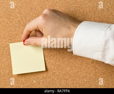 Business man pinning empty yellow sticky paper memo note on cork board with copy space Stock Photo