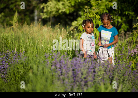 Two young sisters hang out in an urban community garden on a sunny summer evening. Stock Photo