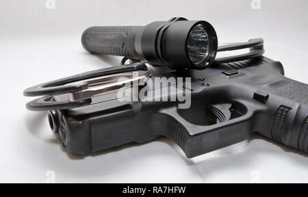 A pair of black and silver handcuffs with a black flashlight laying on top of a black semi automatic pistol on a white background Stock Photo