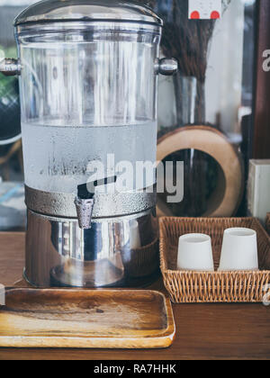 Cold drinking water on cooler with paper cup on weave tray on wooden table service for customer in cafe vertical style. Stock Photo