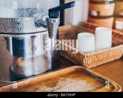 Close-up faucet with water drop on cold drinking water cooler with paper cup on weave tray on wooden table service for customer in cafe. Stock Photo