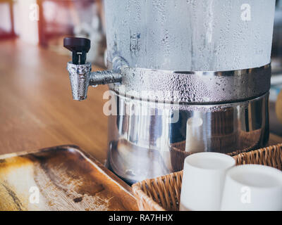 Close-up faucet with water drop on cold drinking water cooler with paper cup on weave tray on wooden table service for customer in cafe. Stock Photo