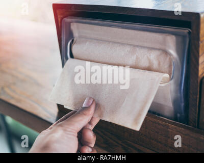 Hand picking brown napkin from the box on wooden tray on wooden table in coffee shop. Stock Photo
