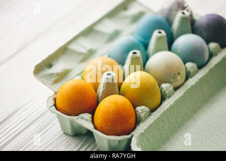 Stylish easter eggs in carton tray on white wooden background. Modern colorful easter eggs painted with natural dye in different colors. Happy Easter, Stock Photo