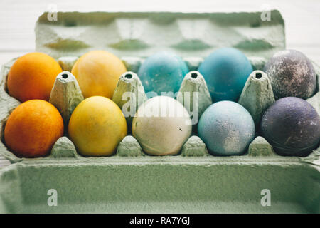 Stylish easter eggs in carton tray on white wooden background. Modern colorful easter eggs painted with natural dye in different colors. Happy Easter, Stock Photo