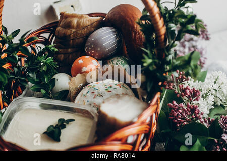 happy easter. easter basket with cake and eggs ham food. colorful decorated egg with floral and chicken ornaments and lilac flowers. space for text.   Stock Photo