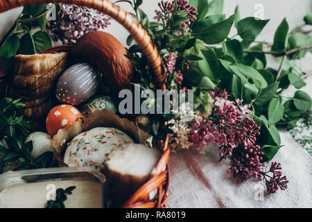 happy easter. easter basket with cake and eggs ham food. colorful decorated egg with floral and chicken ornaments and lilac flowers. space for text.   Stock Photo