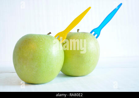 Two green apples with plastic forks on a white wooden table Stock Photo