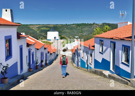 Woman walking along small street in between white washed aligned houses with blue ornaments Stock Photo