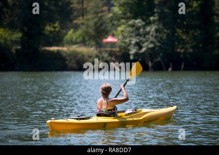 An elderly healthy woman in bathing suit are kayaking on the lake Lacamas in the green forest, actively moving and relaxing at a hot summer day and lo Stock Photo