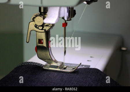 Black fabric under a pressing foot of a sewing machine with double needle. Light blue thread. Stock Photo