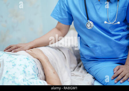 Asian nurse physiotherapist doctor care, help and support senior or elderly old lady woman patient lie down in bed at hospital ward : healthy strong. Stock Photo