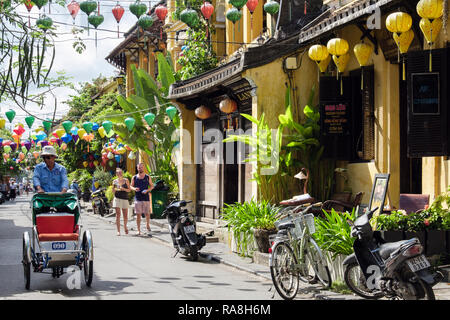 Narrow shopping street with lanterns hanging in historic old quarter with cyclo rickshaw. Hoi An, Quang Nam Province, Vietnam, Asia Stock Photo