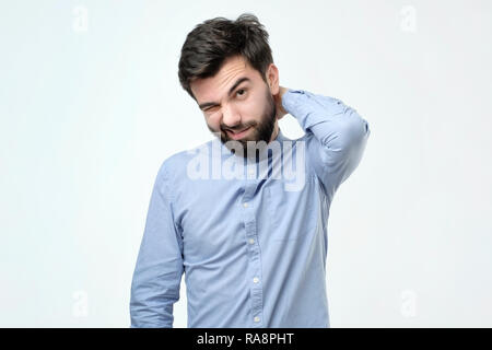 Maybe I should say sorry for my behaviour. Hispanic man with beard looking with puzzled expression, scratching head, being clueless Stock Photo