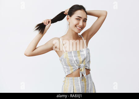 Woman feeling happy hair finally got strong and beautiful. Portrait of pleased carefree stylish female coming ponytail and smiling joyfully, making up hairstyle while preparing go out Stock Photo
