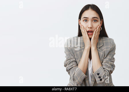 Waist-up shot of stunned speechless cute woman in fashionable jacket over white t-shirt, gasping, staring surprised and impressed at camera, holding palms on cheeks, being amazed with rumors Stock Photo