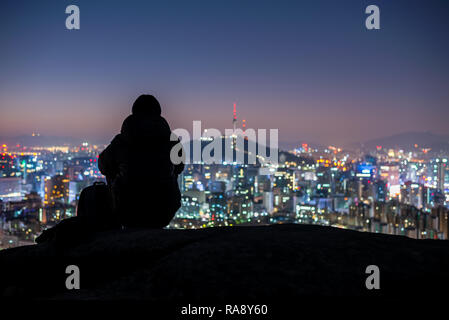 Young man traveler sitting on the rock looking Seoul city at Night,South Korea Stock Photo